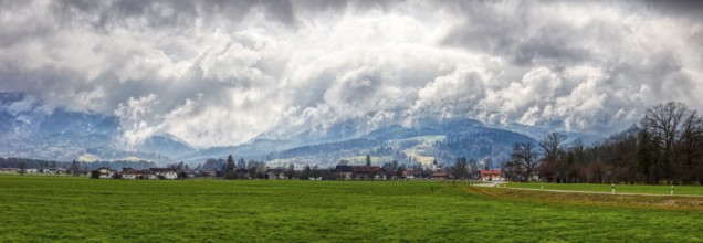Green meadow and small village in the foreground, dramatic clouds, mountains in the background, Bad