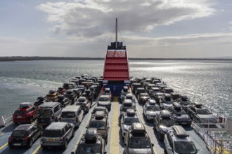 Ferry loaded with cars, sun reflected on the sea, bright sky in the background, Rosslare Harbour