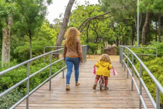 Rear view of a caucasian mother and little girl walking and cycling on a park