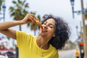 Latin woman with curly hair enjoying take away pizza in the street