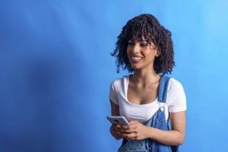 Young woman smiling while using a smartphone against a vibrant blue background, showcasing a modern
