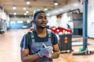 Confident young mechanic wearing gloves and protective glasses stands in a professional auto repair