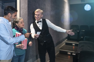 Movie theater usher showing seats to a couple holding popcorn buckets, ready to enjoy the film