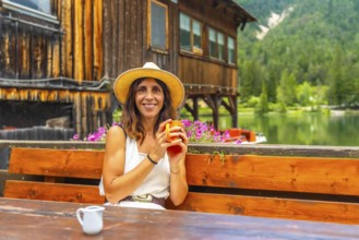 Woman with straw hat enjoying a hot drink in a bar with mountain lake view in the dolomites