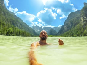 Tourist gesturing thumbs up while swimming in the turquoise water of lago di landro, surrounded by
