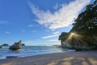 Landscape with sandy beach and bright sun behind rocks by the sea, Cathedral Cove, Coromandel,