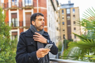 Businessman in warm winter clothes using smartphone standing in the city
