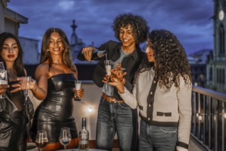 Man serving champagne in glasses to multi-ethnic friends in a night party in a roof
