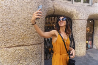 Smiling woman taking selfie with smartphone in front of casa mila in barcelona, enjoying summer