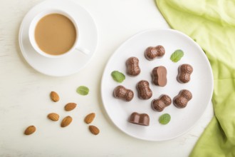 Chocolate candies with almonds and a cup of coffee on a white wooden background and green textile.