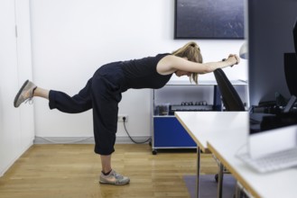 A woman does sports exercises at her workplace in an office in Berlin, 08/08/2024