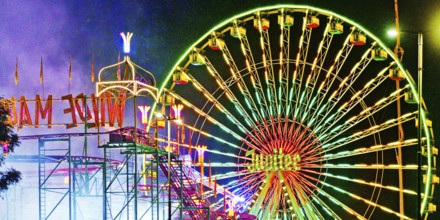 Cranger Kirmes with colourfully illuminated fairground rides and the Ferris wheel at night, Herne,