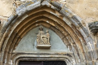 Sculpture of Pieta is prominently displayed above the portal of the church in Collanges, Puy de