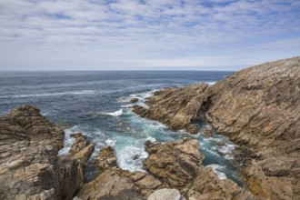 Rocky west coast of the Quiberon peninsula in Brittany, France, with a partly cloudy sky. Crashing