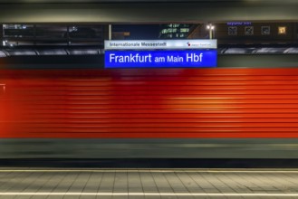 Central station in the evening. Station sign with passing train. Motion blur. Frankfurt am Main,
