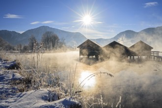 Boat huts in the morning light in front of mountains, lake, snow, winter, sunbeams, fog, Lake