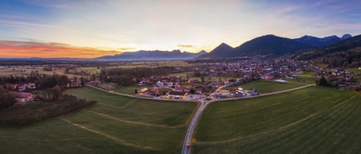 Panoramic view of a village in a wide green plain with mountains in the background at dusk, Bad
