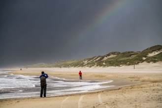 Walkers on the beach, dark storm clouds, choppy sea, autumn on the North Sea in North Holland,