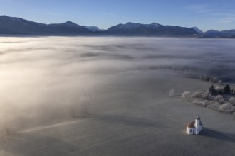 Aerial view of a chapel in front of mountains in winter, hoarfrost, morning light, fog, view of the