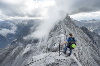 Mountaineer on a narrow rocky ridge on a steel cable, Watzmann crossing to Watzmann Mittelspitze,
