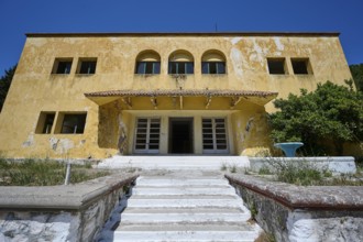 An abandoned building with a crumbling façade and an external staircase on a sunny day under a blue