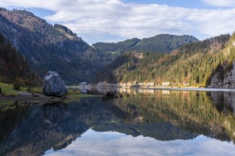 The Vordere Gosausee in autumn with a view of the Gasthof Gosausee. On the left a large rock on the