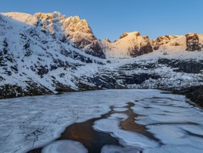 Aerial view of icy lake in front of steep mountains, winter, sunrise, Storvatnet, Flakstadoya,