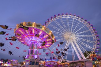 A lively funfair at dusk, illuminated by a large Ferris wheel and a colourful chain carousel,
