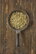 A skillet filled with sauteed diced mushrooms mixed with fresh herbs on a rustic wooden table. The
