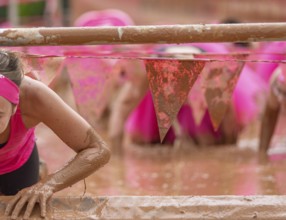 Participant climbs through muddy obstacles in a sporting competition