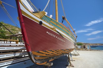 A colourful wooden boat hangs in a dry dock under a clear blue sky and calm atmosphere, Patmos