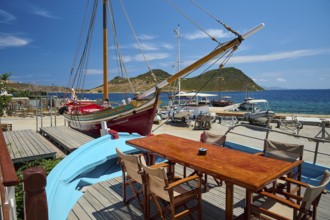 A harbour scene with wooden boats and a table with chairs and a blue boat in the foreground in
