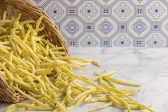 A basket of yellow beans tipped out on a marble worktop