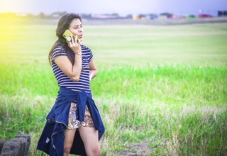 Young girl calling phone on the field. Beautiful young woman calling by phone outdoors