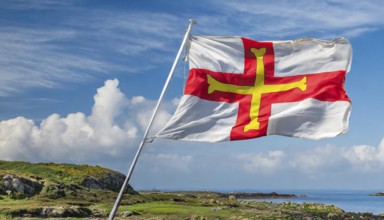 The flag of the Isle of Guernsey, Great Britain, flutters in the wind