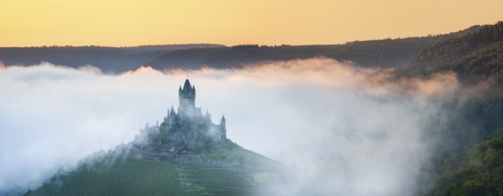 View of the Reichsburg Cochem with morning mist in the Moselle valley, Cochem,