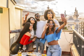 Multiracial friends taking selfie during party in a rooftop during sunset