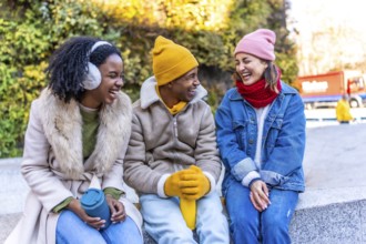 Three cheerful multi ethnic young friends are sitting and laughing together in the city during a