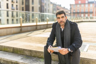 Casual caucasian businessman sitting in the city with notebook on hands in a sunny day of winter