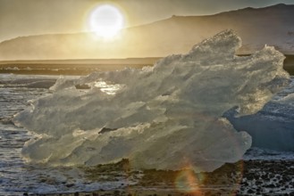 Backlit block of ice, beach at glacier lagoon Jökulsarlon, Breiðamerkursandur, south coast,