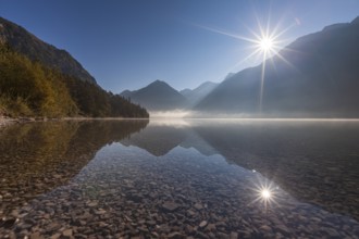 Foggy mood and reflection of mountains in mountain lake, sun star, backlight, morning light,