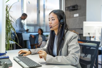 Young asian businesswoman wearing headset working with computer in a modern coworking office,