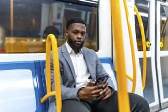 Young businessman sitting on a subway train, using a smartphone during his daily commute, staying