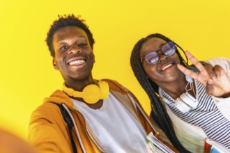 Studio portrait with yellow background of African students taking selfie and gesturing success with