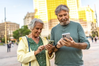 Happy caucasian casual senior couple using phone standing in an urban square