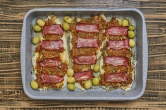 Roasted fish fillets are layered with bacon and herb sauce, accompanied by green olives. This