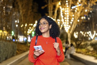 Smiling student walking in a decorated city using her smartphone during christmas holidays