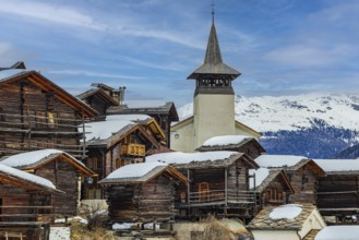 Old wooden houses with snow-covered roofs and the Saint Theodule church in the historic village