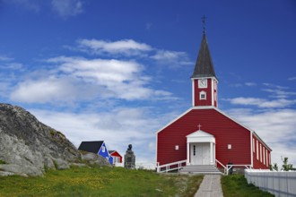 Red church with white entrance and tower, sculpture next door under a blue sky, Church of the