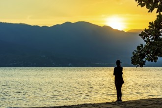 Woman standing in front of the sea during sunset in Ilhabela on the north coast of São Paulo, Sao